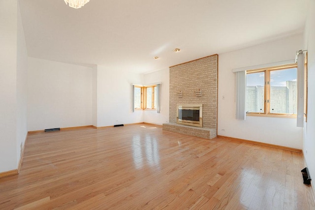 unfurnished living room featuring light wood-style floors, a brick fireplace, visible vents, and baseboards