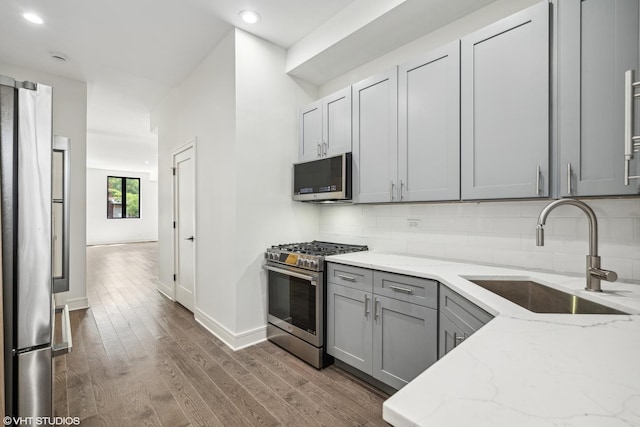 kitchen with light stone countertops, appliances with stainless steel finishes, dark hardwood / wood-style flooring, gray cabinetry, and sink