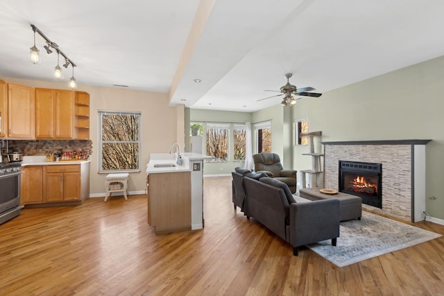 living room featuring ceiling fan, a fireplace, light hardwood / wood-style floors, and sink