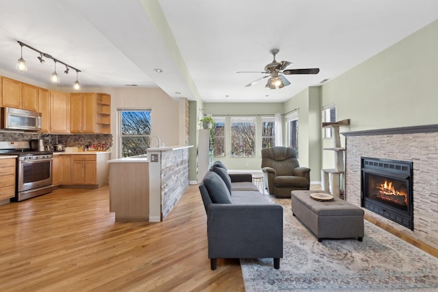 living room with light hardwood / wood-style floors, a stone fireplace, ceiling fan, and sink