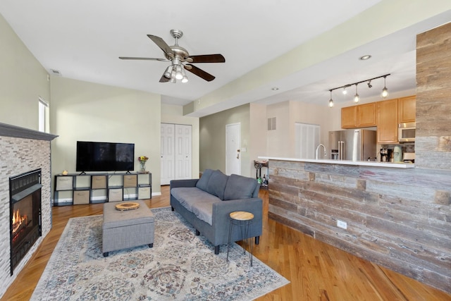 living room featuring track lighting, ceiling fan, sink, light hardwood / wood-style floors, and a stone fireplace