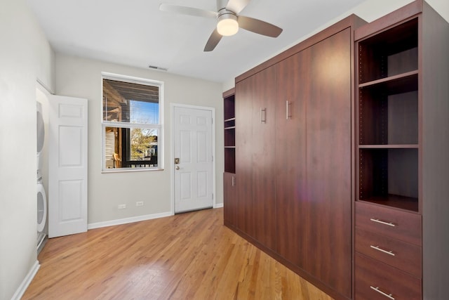 unfurnished bedroom with stacked washer / dryer, ceiling fan, and light wood-type flooring