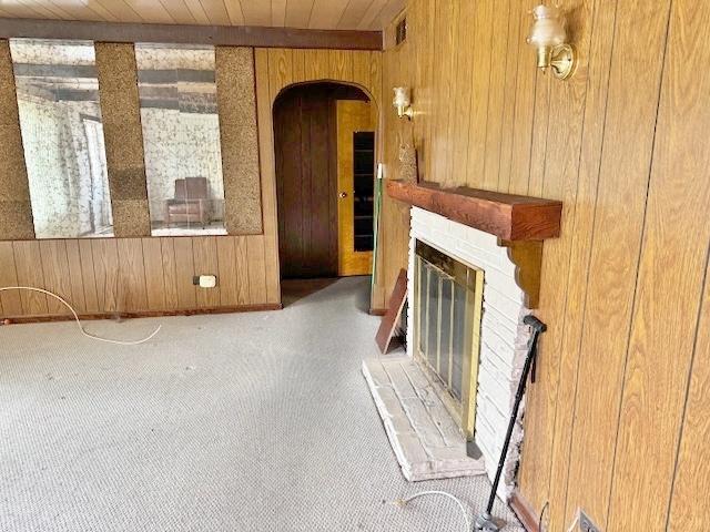1429 N Wolf Rd, Berkeley, IL 60163 - unfurnished living room featuring wood walls, a brick fireplace, arched walkways, wood ceiling, and carpet floors