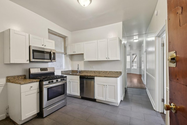 kitchen with appliances with stainless steel finishes, dark hardwood / wood-style floors, white cabinetry, and dark stone countertops