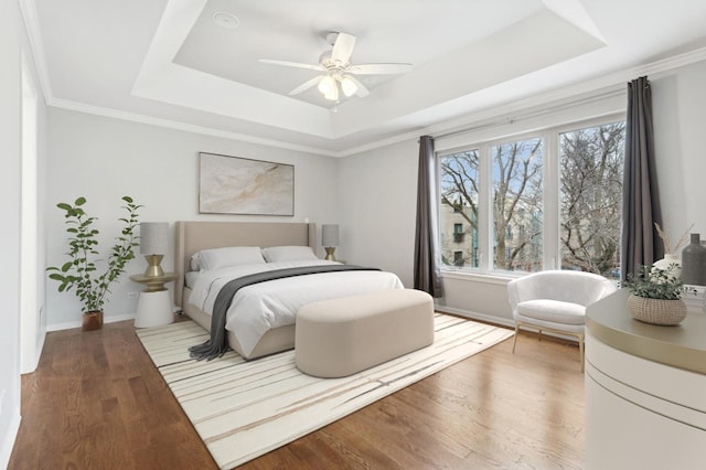 bedroom featuring a raised ceiling, wood finished floors, baseboards, a ceiling fan, and crown molding