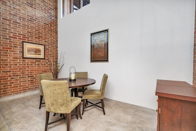 dining room featuring a towering ceiling and brick wall