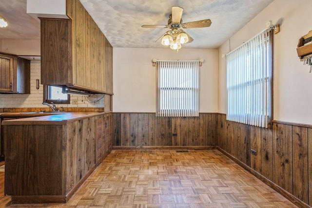 kitchen featuring kitchen peninsula, backsplash, sink, light parquet flooring, and wood walls