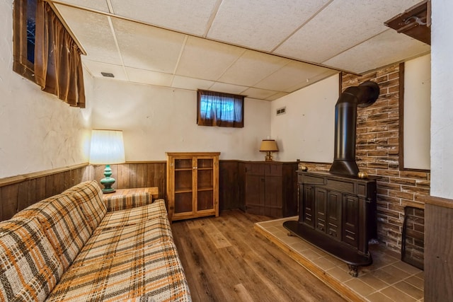 living room featuring a paneled ceiling, wooden walls, a wood stove, and hardwood / wood-style flooring