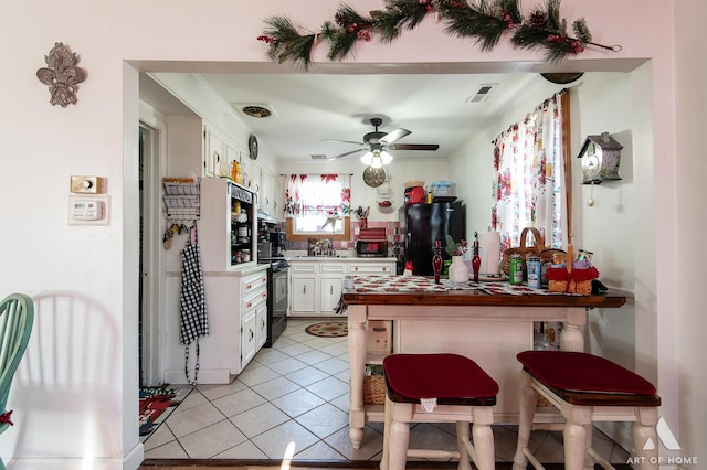 kitchen featuring white cabinetry, black fridge, ceiling fan, and light tile patterned flooring