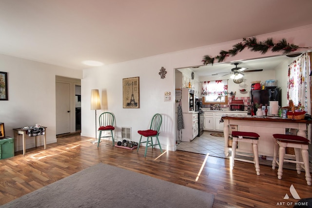 interior space with white cabinetry, a kitchen breakfast bar, black fridge, crown molding, and light hardwood / wood-style floors