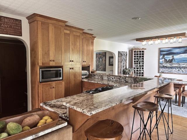 kitchen featuring a kitchen bar, stone countertops, light hardwood / wood-style flooring, and stainless steel microwave