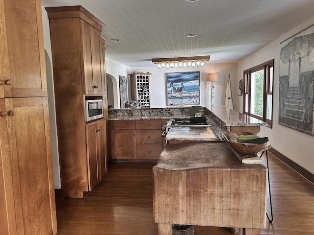 kitchen featuring dark wood-type flooring, a kitchen breakfast bar, kitchen peninsula, a textured ceiling, and appliances with stainless steel finishes