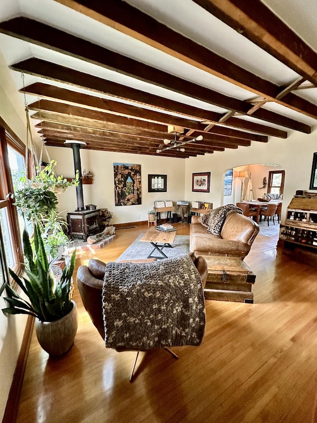 living room with beamed ceiling, hardwood / wood-style floors, and a wood stove