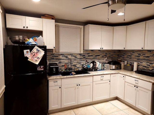 kitchen featuring black refrigerator, light stone counters, white cabinetry, and sink