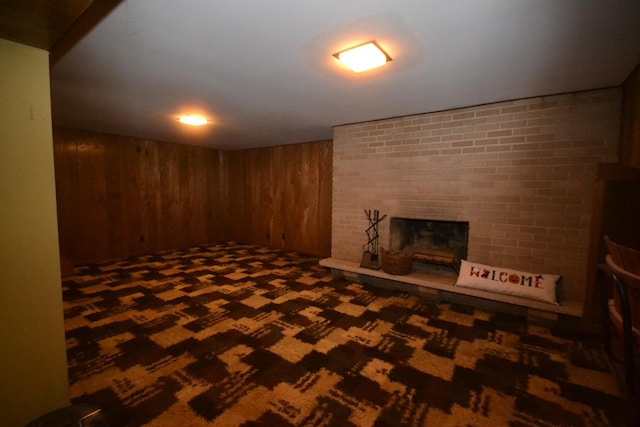 finished below grade area with dark carpet, wood walls, and a brick fireplace