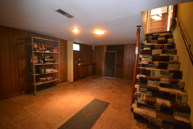 basement featuring visible vents, wood walls, and stairs