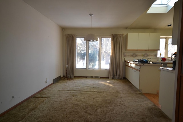 kitchen featuring light carpet, a skylight, visible vents, white cabinets, and decorative light fixtures