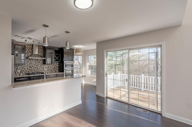 kitchen with dark hardwood / wood-style flooring, hanging light fixtures, a healthy amount of sunlight, and wall chimney range hood