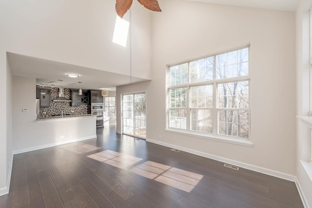 unfurnished living room with high vaulted ceiling, ceiling fan, and dark wood-type flooring