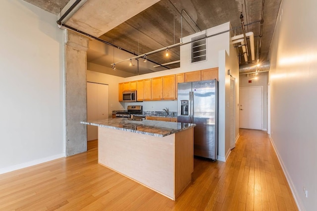 kitchen with dark stone counters, track lighting, light hardwood / wood-style flooring, a kitchen island, and stainless steel appliances