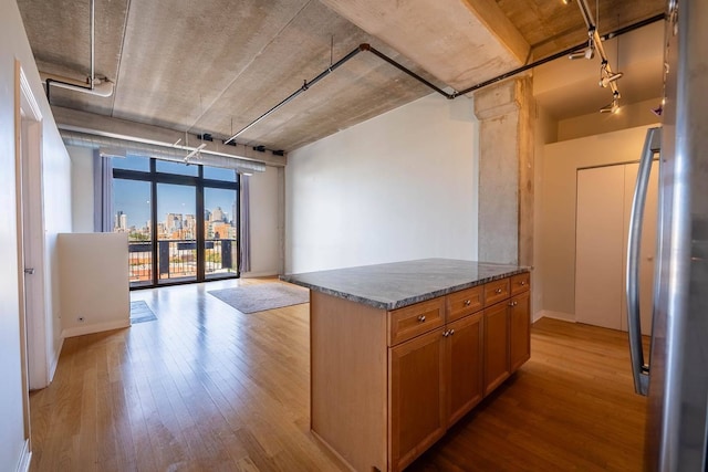 kitchen with a center island, rail lighting, light hardwood / wood-style flooring, stainless steel fridge, and dark stone counters