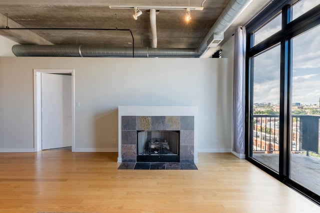 unfurnished living room featuring light wood-type flooring, a tile fireplace, and track lighting