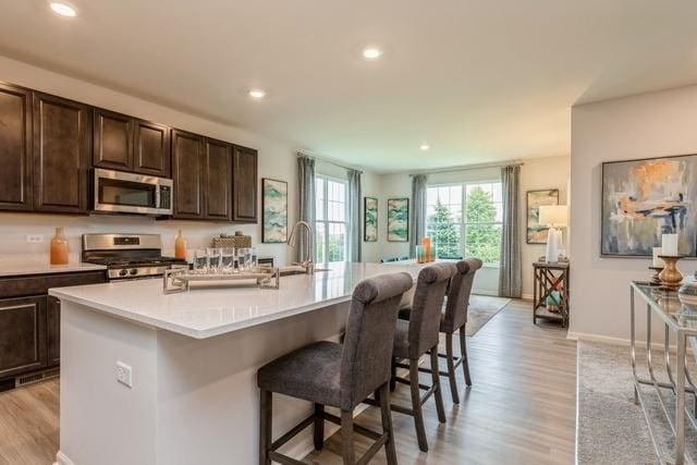 kitchen with appliances with stainless steel finishes, light wood-type flooring, a kitchen bar, and a center island with sink