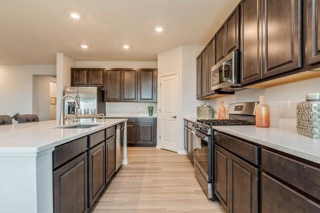 kitchen featuring sink, light hardwood / wood-style floors, dark brown cabinets, a kitchen island with sink, and appliances with stainless steel finishes