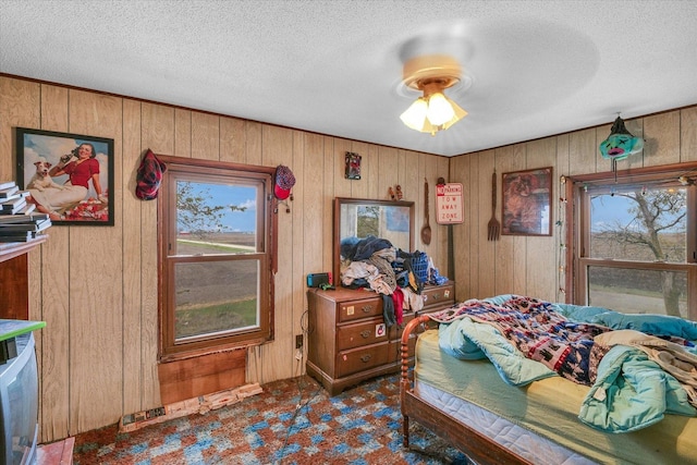 bedroom with a textured ceiling, ceiling fan, and wood walls