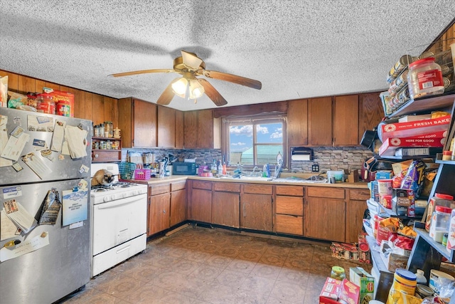 kitchen featuring stainless steel refrigerator, ceiling fan, white gas range, tasteful backsplash, and a textured ceiling