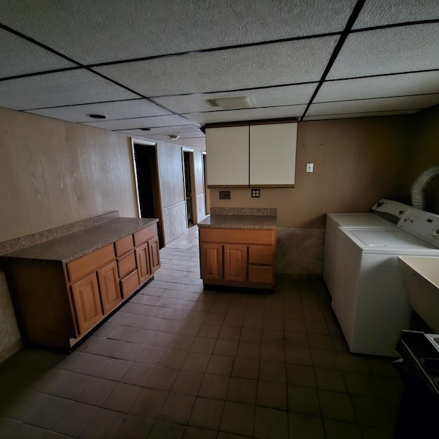 laundry area featuring tile patterned floors, separate washer and dryer, wood walls, and cabinets