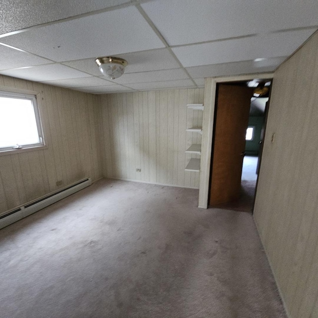 carpeted spare room with a paneled ceiling, wood walls, and a baseboard radiator