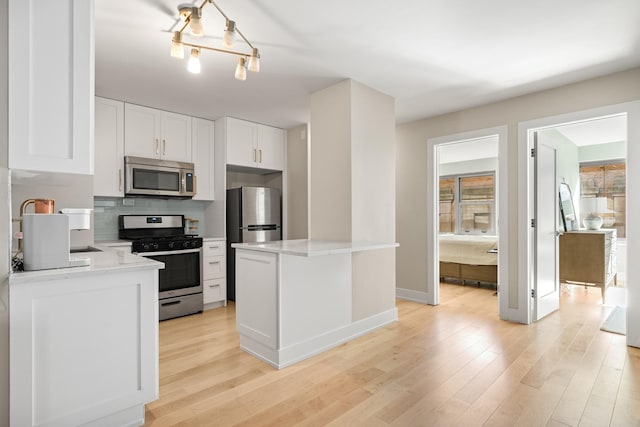 kitchen featuring decorative backsplash, white cabinets, stainless steel appliances, and light wood-type flooring