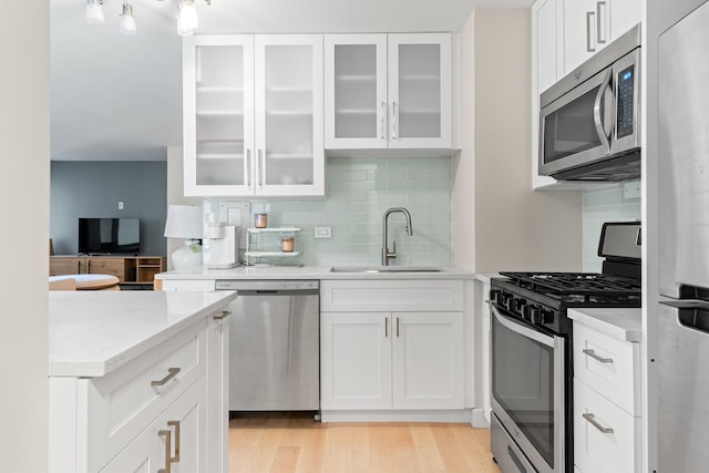 kitchen featuring light stone countertops, sink, stainless steel appliances, light hardwood / wood-style floors, and white cabinets