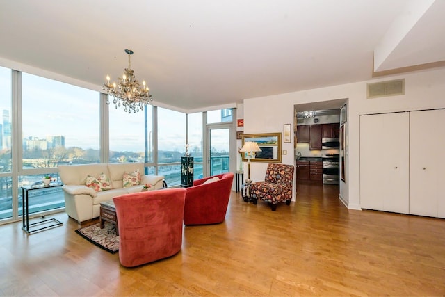 living room featuring expansive windows, a water view, light wood-type flooring, and an inviting chandelier