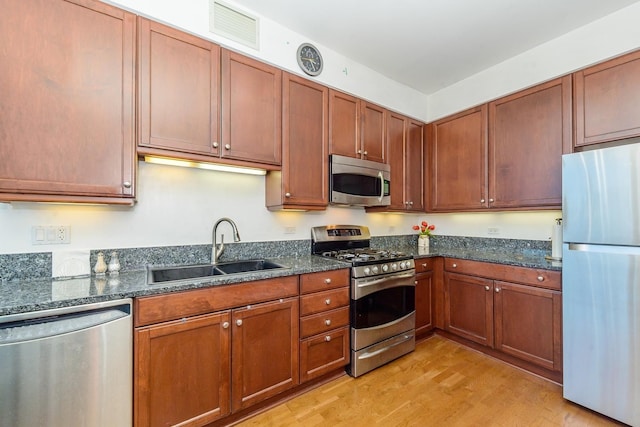 kitchen featuring dark stone counters, sink, stainless steel appliances, and light wood-type flooring