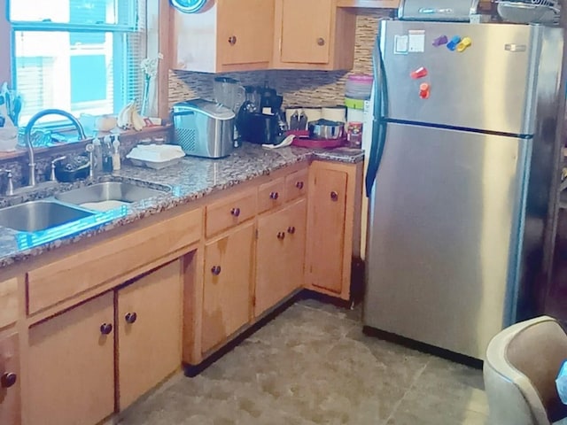 kitchen with backsplash, stainless steel fridge, light stone countertops, and sink