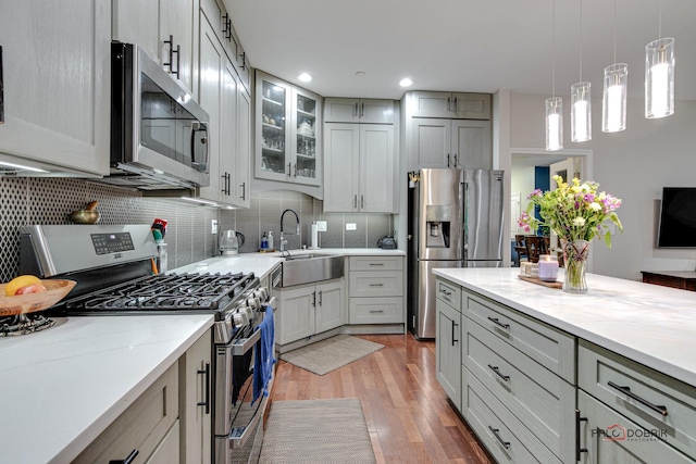 kitchen with appliances with stainless steel finishes, light stone counters, sink, decorative light fixtures, and gray cabinets