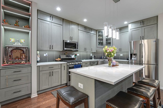 kitchen featuring stainless steel appliances, dark hardwood / wood-style floors, a kitchen island, hanging light fixtures, and a breakfast bar area