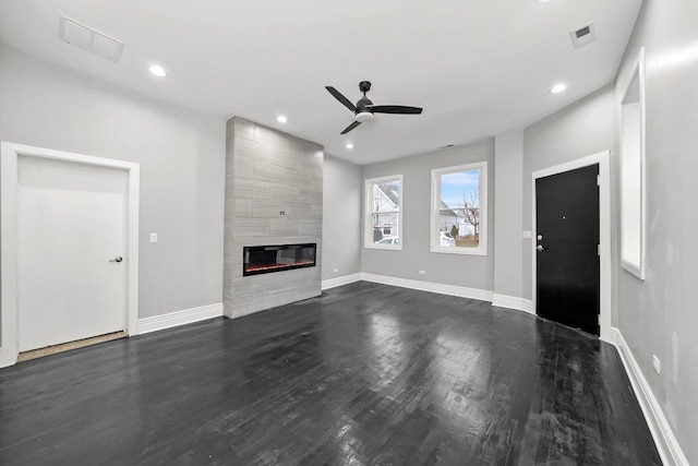 unfurnished living room with a tiled fireplace, ceiling fan, and dark wood-type flooring