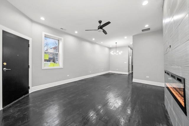 unfurnished living room featuring a tiled fireplace, dark hardwood / wood-style flooring, and ceiling fan with notable chandelier