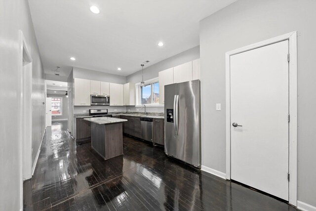 kitchen with pendant lighting, a center island, white cabinets, dark hardwood / wood-style flooring, and stainless steel appliances