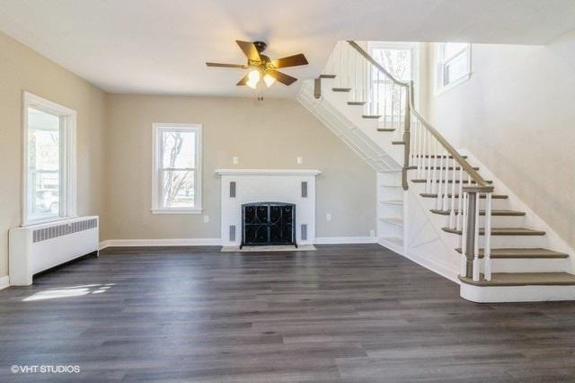 unfurnished living room with ceiling fan, radiator heating unit, and dark wood-type flooring