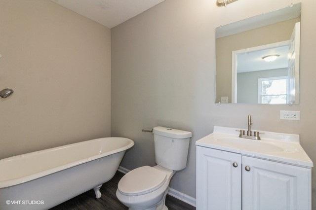 bathroom featuring vanity, a tub to relax in, and toilet