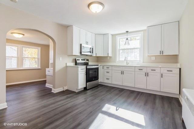 kitchen with radiator, stainless steel appliances, dark wood-type flooring, white cabinetry, and hanging light fixtures