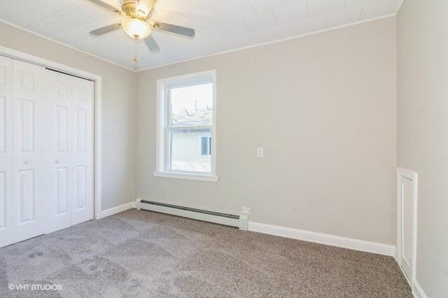 unfurnished bedroom featuring baseboard heating, ceiling fan, a closet, and light carpet