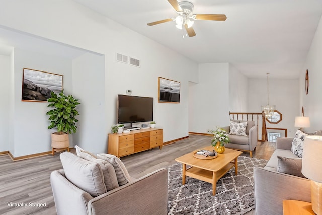 living room featuring lofted ceiling, wood-type flooring, and ceiling fan with notable chandelier