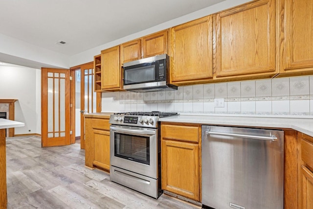 kitchen with light wood-type flooring, appliances with stainless steel finishes, and tasteful backsplash