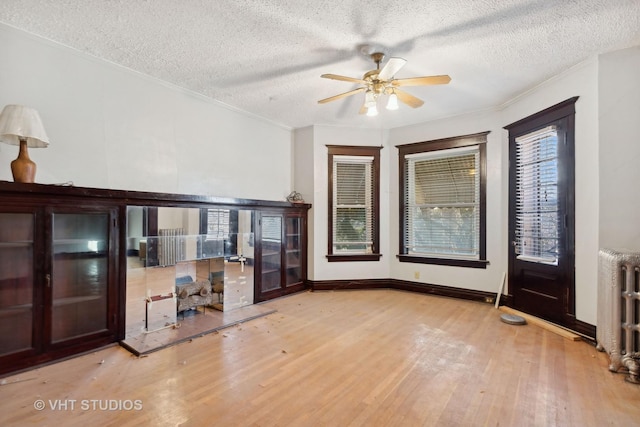 interior space featuring ceiling fan, light wood-type flooring, radiator heating unit, and a textured ceiling