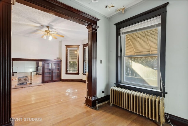 unfurnished room with decorative columns, radiator, a textured ceiling, and hardwood / wood-style flooring